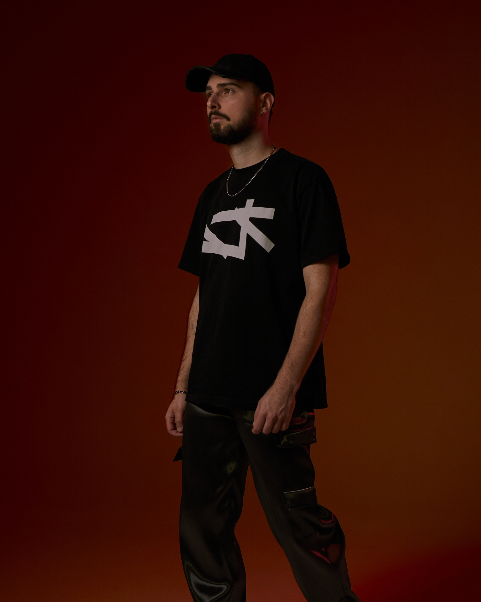 RH4DEZ walking against a deep red backdrop wearing a black RH4DEZ tee and cap